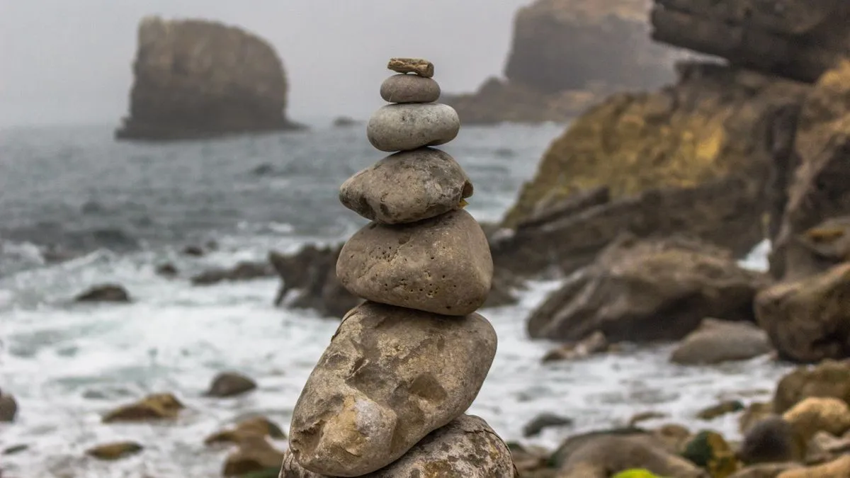 The three-fund portfolio, adapted for non-US investors A cairn of stacked stones stands on a rocky shoreline while waves break against misty cliffs behind it.